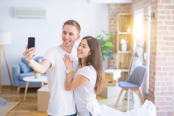 Young beautiful couple standing using smartphone to take a selfie at new home around cardboard boxes