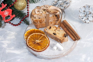 Traditional Italian biscotti or cantuccini cookies on a round white wooden board with cinnamon, dried orange slices and marshmallows on a light table near a Christmas tree. Christmas baking concept