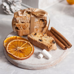 Traditional Italian biscotti or cantuccini cookies on a round white wooden board with cinnamon, dried orange slices and marshmallows on a light table near a Christmas tree. Christmas baking concept