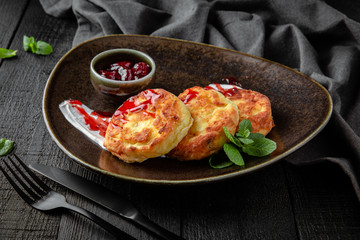 A healthy nutritious dietary breakfast of cottage cheese pancakes with cherries in their own juice and sour cream.  Restaurant menu. Background black boards.