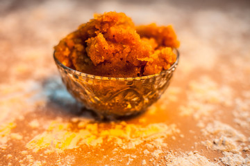 Close up of Indian Gujarati popular dish Atte ka sheera or Halwa-Karah parshad in a glass bowl on brown surface with some spread wheat flour. Horizontal shot. - obrazy, fototapety, plakaty