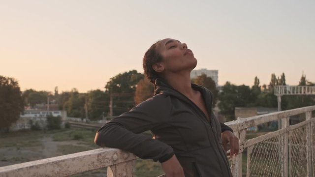 Calm Athletic African American Woman In Sportswear Leaning On Railing While Working Out On Old Bridge