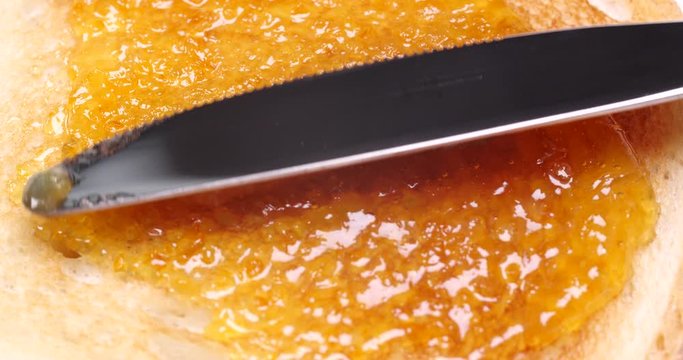 Spreading of delicious orange jam onto crispy toast, closeup