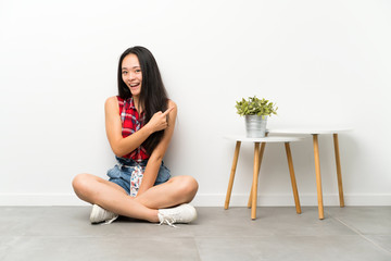 Teenager asian girl sitting on the floor pointing finger to the side