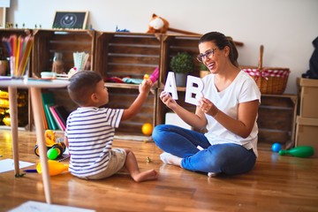 Beautiful teacher teaching alphabet to student toddler boy at kindergarten