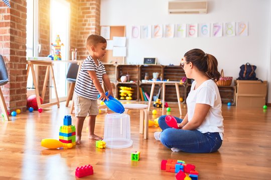 Beautiful teacher and toddler boy playing drum using skitlle and plastic basket at kindergarten