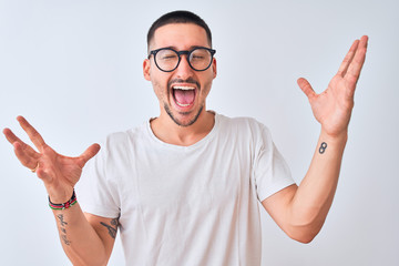 Fototapeta premium Young handsome man wearing glasses and standing over isolated background celebrating crazy and amazed for success with arms raised and open eyes screaming excited. Winner concept