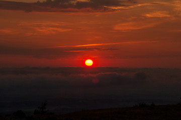 red sun in a glowing sky over a sea of clouds