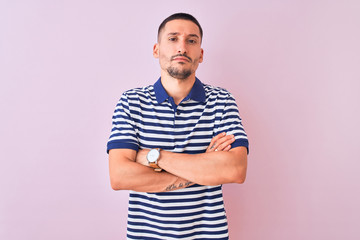 Young handsome man wearing nautical striped t-shirt over pink isolated background skeptic and nervous, disapproving expression on face with crossed arms. Negative person.