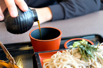 Fototapeta na wymiar Man pour a cold sauce for dipped in cold soba (buckwheat noodles)