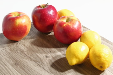 Red apples, yellow lemons on a wooden board against a white background.