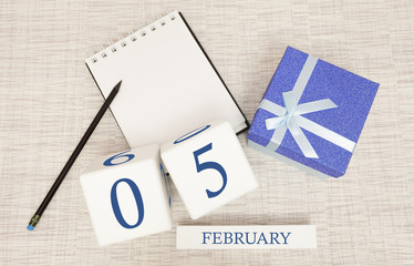 Calendar with trendy blue text and numbers for February 5 and a gift in a box.