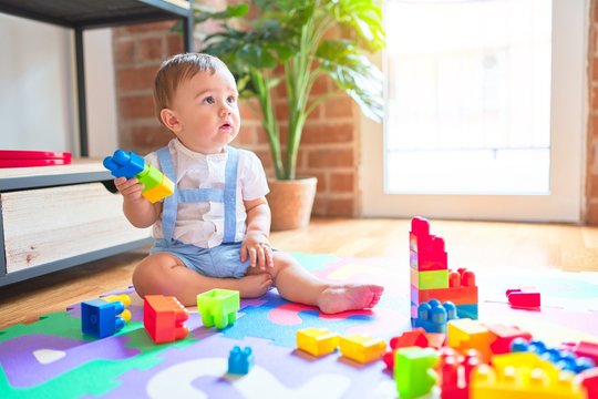 Beautiful toddler sitting on puzzle carpet playing with building blocks at kindergarten