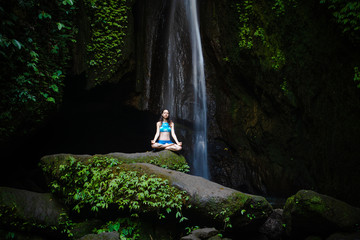 Young Caucasian woman meditating, practicing yoga at waterfall. Gyan mudra. Leke Leke waterfall, Bali, Indonesia.