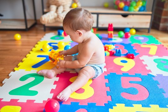 Beautiful toddler sitting on puzzle carpet playing with building blocks at kindergarten
