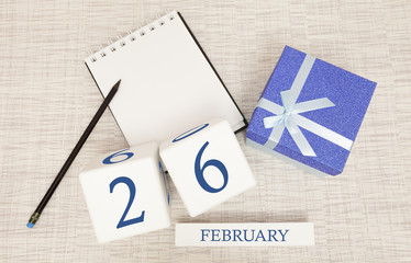Calendar with trendy blue text and numbers for February 26 and a gift in a box.