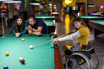 Disabled girl in a wheelchair playing billiards with friends