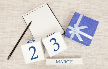 Calendar with trendy blue text and numbers for March 23 and a gift in a box.