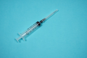 Empty syringe with needle on a turquoise background. Medical background. Treatment for a patient. Drug addict concept photo. Copy space.