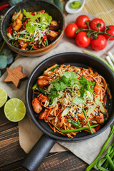 Bowl of stir fried udon noodles garnished with black sesame seeds and fresh mint with green chopsticks