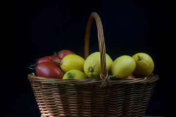 wicker basket with autumn fruits and lemons on black background