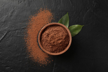 Bowl with cocoa powder and leaves on black background, top view