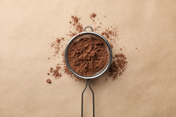 Strainer with cocoa powder on cardboard background, top view