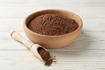 Wooden bowl and scoop with cocoa powder on white wood background, closeup