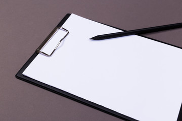 Clipboard with a white sheet and pen on a gray-dark background. View from above. space for text