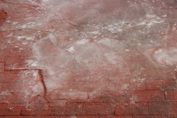Pavement cobbled with red stone covered with melting broken ice