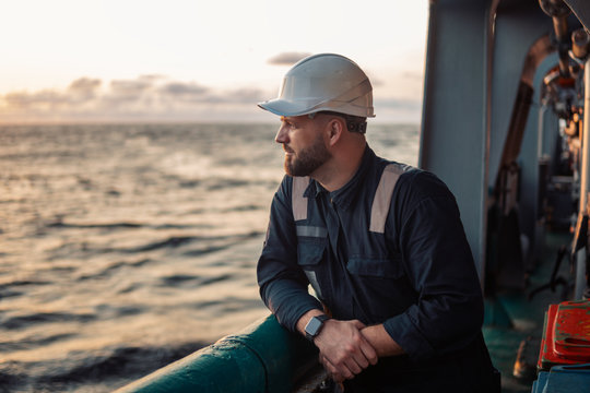 Marine Deck Officer or Chief mate on deck of offshore vessel or ship , wearing PPE personal protective equipment - helmet, coverall. He holds VHF walkie-talkie radio in hands.