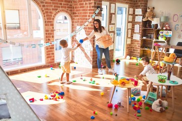 Beautiful teacher and toddlers playing basketball using balls and wicker basket  around lots of toys at kindergarten