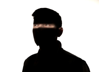 Dramatic portrait of caucasian young man in the dark isolated on white studio background. Sunlight line on the dark face. Human nature, hidden things, psycology concept. Art elegant creative photo.