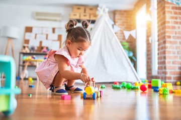 Young beautiful toddler sitting on the floor playing with wooden train toy at kindergaten