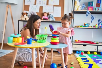 Young beautiful teacher and toddler building pyramid using hoops on the table at kindergarten