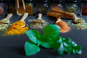 Spices and herbs of various colors in wooden spoons on black slate stone