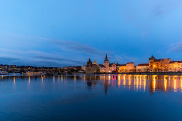 Fototapeta na wymiar The center of Prague Czech Republic and its biggest landmark on the Vltava river Charles Bridge and the beautiful waterfront illuminated during Christmas at sunset with reflections of lights.