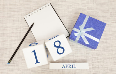 Calendar with trendy blue text and numbers for April 18 and a gift in a box.