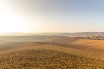 View of plowed land after the season in the Moravian Tuscany region's landscape full of ripples overlooking the village in the background during an afternoon sunny day without clouds