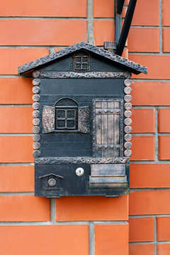 Vintage metallic bronze mailbox in shape of little house with window and door hanging on the brick wall