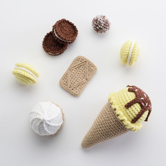 Cute homemade amigurumi toys flat lay. Knitted lemon and chocolate ice cream, macarons and cookies on white background