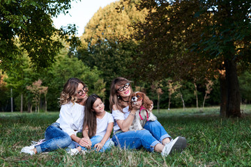 Two young blond women and one brunette girl, wearing jeans and white t-shirts, sitting on green...