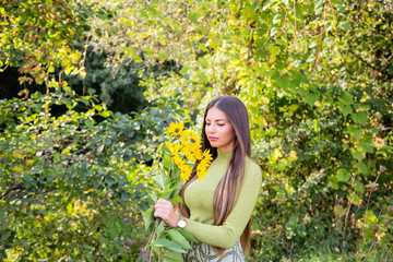 Outdoors portrait of beautiful young brunette woman with long hair and flowers in the park