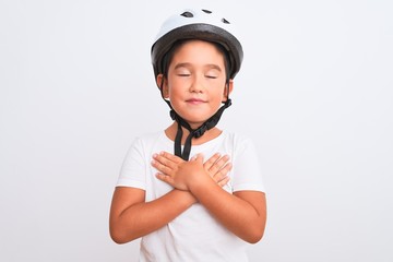 Beautiful kid boy wearing bike security helmet standing over isolated white background smiling with hands on chest with closed eyes and grateful gesture on face. Health concept.