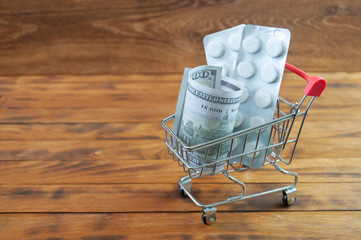 Shopping cart with tablet blisters and dollar banknote. Spending money on pills and expensiveness of medicine concept.