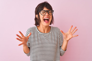 Young beautiful woman wearing striped t-shirt and glasses over isolated pink background celebrating...