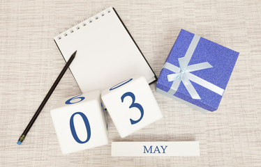 Calendar with trendy blue text and numbers for May 3 and a gift in a box.