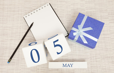 Calendar with trendy blue text and numbers for May 5 and a gift in a box.