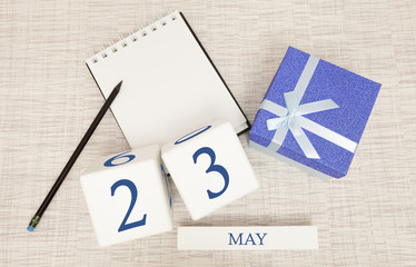 Calendar with trendy blue text and numbers for May 23 and a gift in a box.