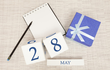 Calendar with trendy blue text and numbers for May 28 and a gift in a box.